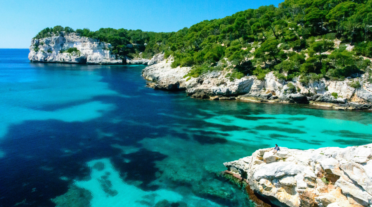 Person sitting on a cliff above the sea in Minorca, Spain