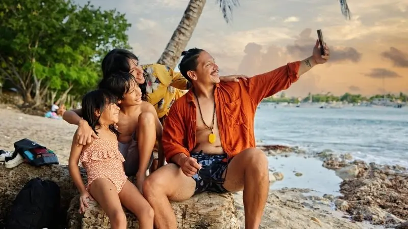 Eine Familie sitzt lächelnd an einem Strand in der Karibik und macht ein Selfie