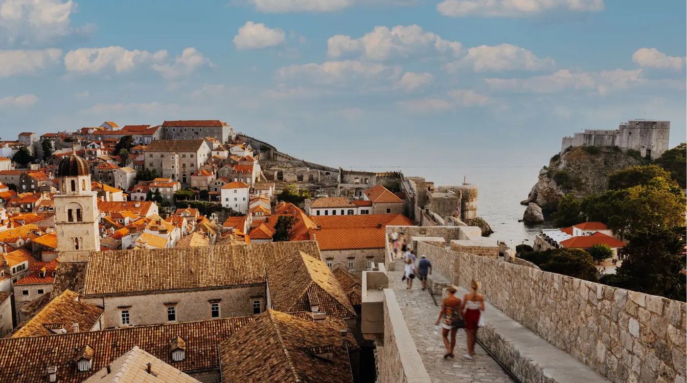 Vista panorâmica das muralhas medievais de Dubrovnik com os telhados alaranjados da Cidade Velha e o Mar Adriático ao fundo, na Croácia.