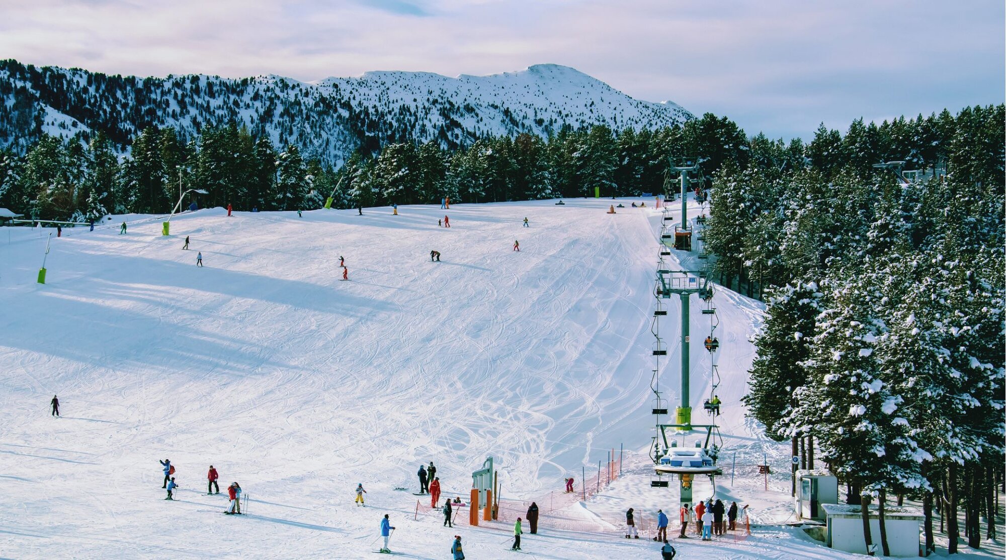 Pista de esquí en Andorra con varios esquiadores bajando y un remonte; paisaje de nieve y bosque.