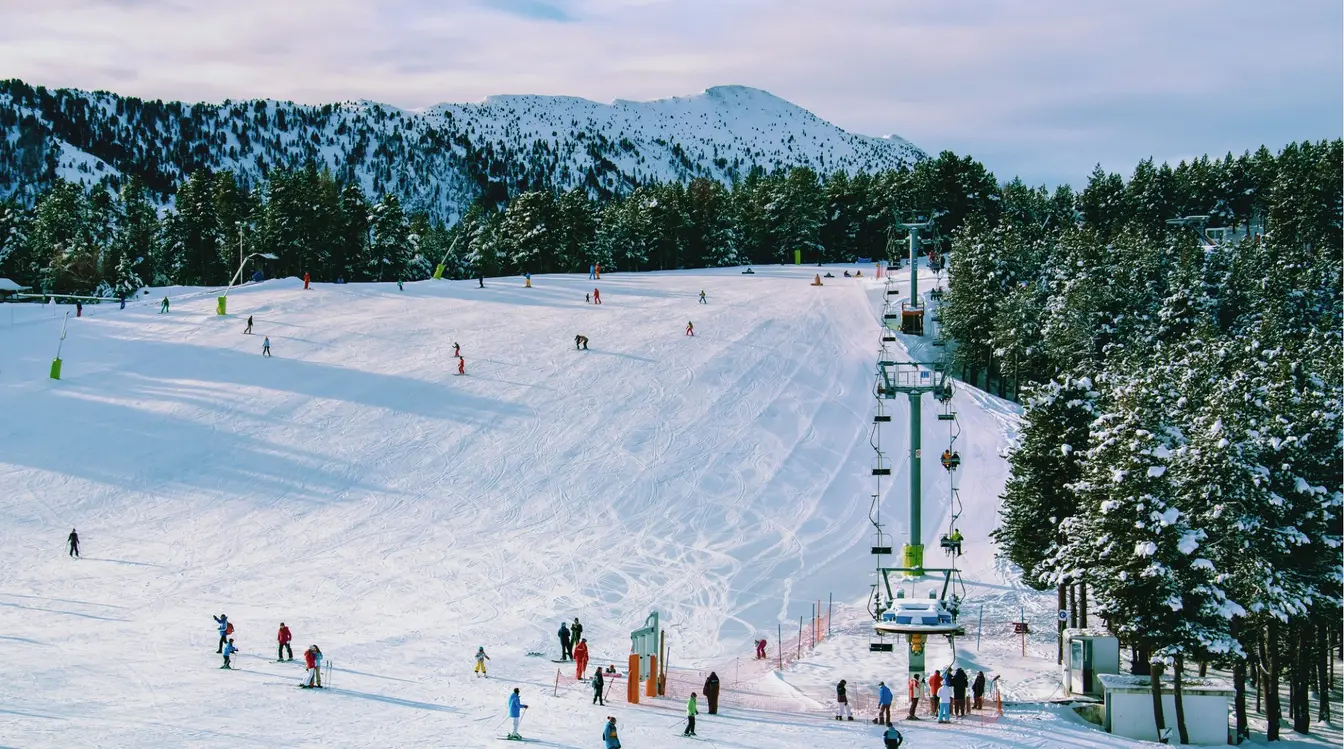 Pista de esquí en Andorra con varios esquiadores bajando y un remonte; paisaje de nieve y bosque.