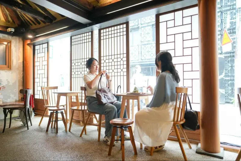 ソウル鍾路区のスタイリッシュなカフェの窓際でデザートを食べながら笑顔で語り合う韓国人女性二人組