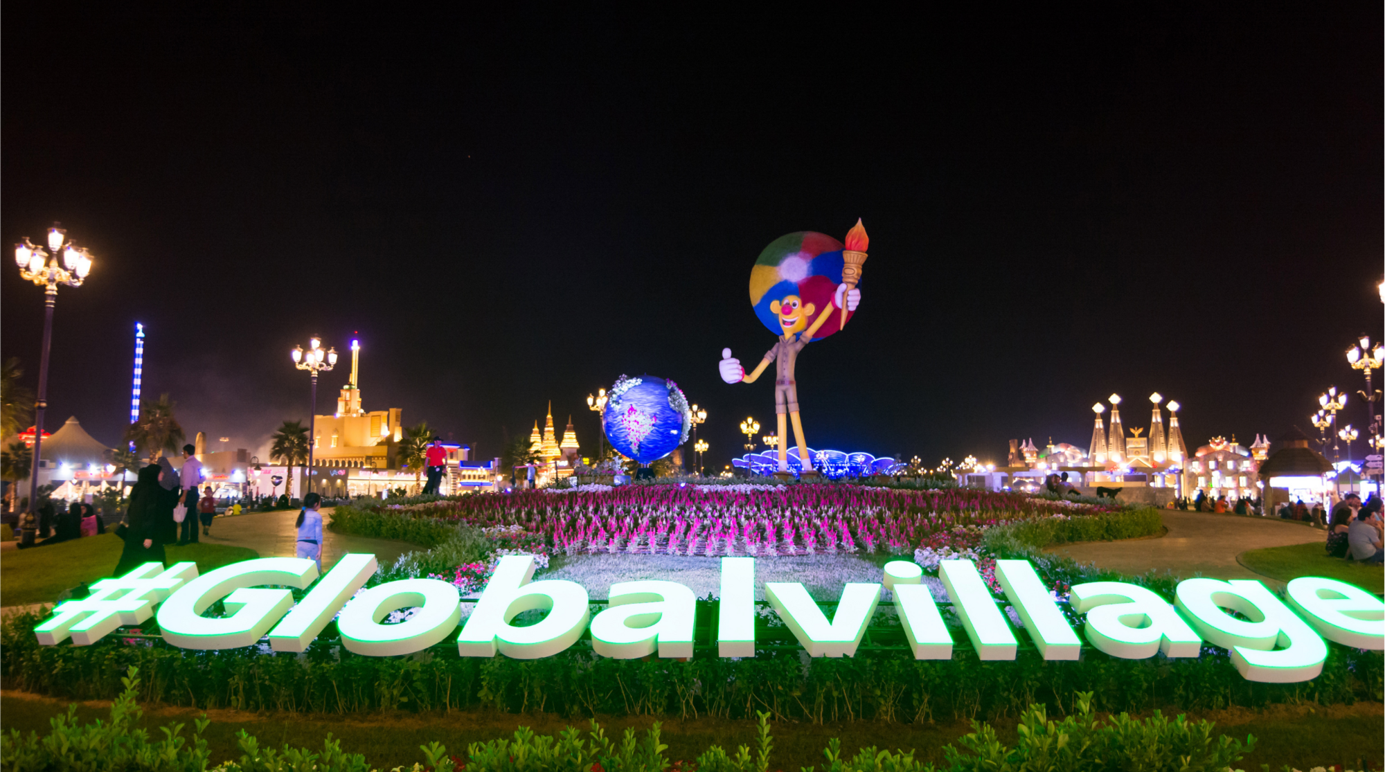 مدخل القرية العالمية دبي ليلًا مع شعار جلوبال فيليدج بالإنجليزية وإضاءة مبهرة وازدحام الزوار في موسم 2025