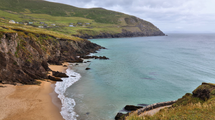 A view from Ireland's Slea Head Cliffs looking over Coumeenoole Beach, with green cliffs and a bright blue sea.