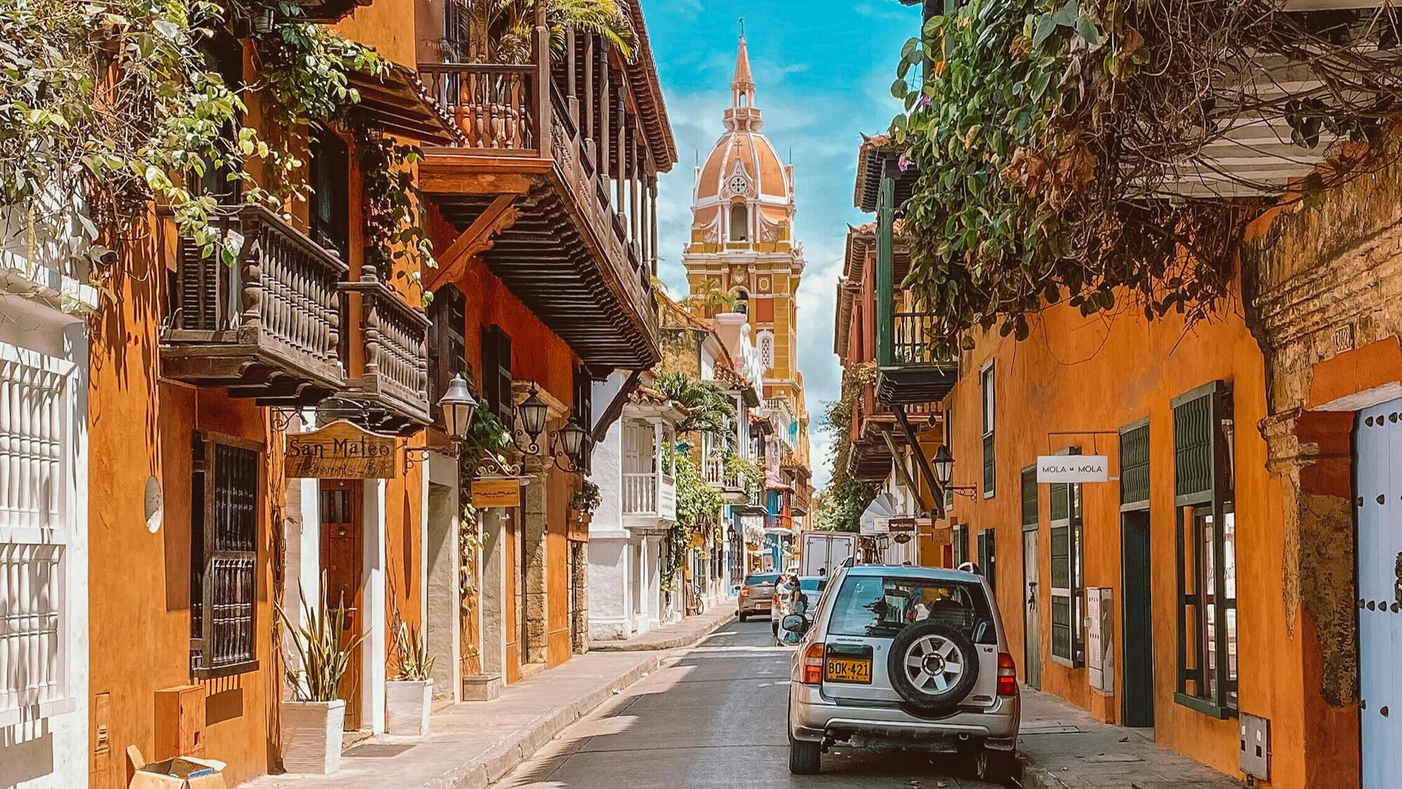 A cozy street in Cartagena lined with shops, cafés, pedestrians, and parked cars