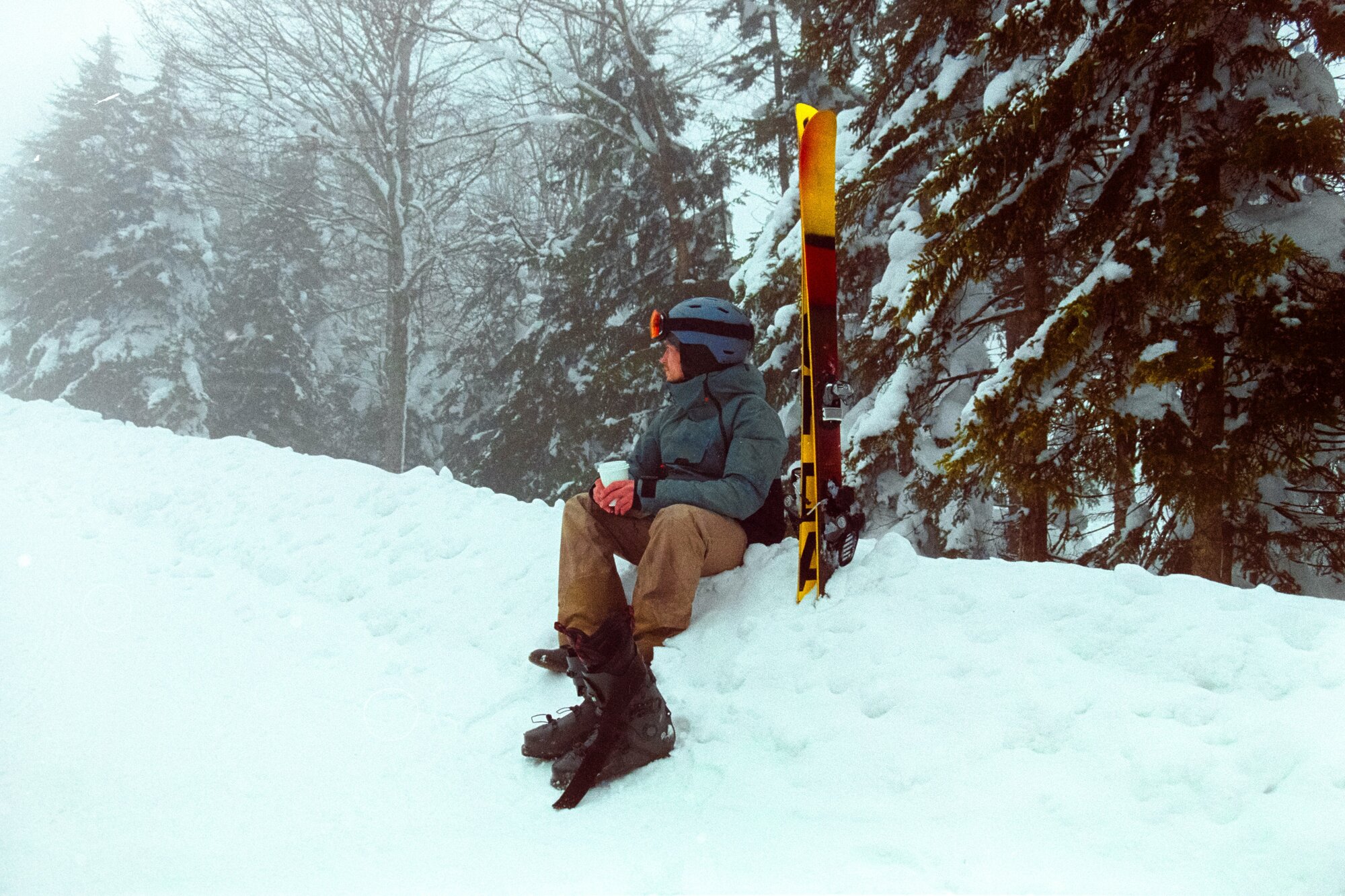 Man sitting in the snow with ski trip equipment and a drink