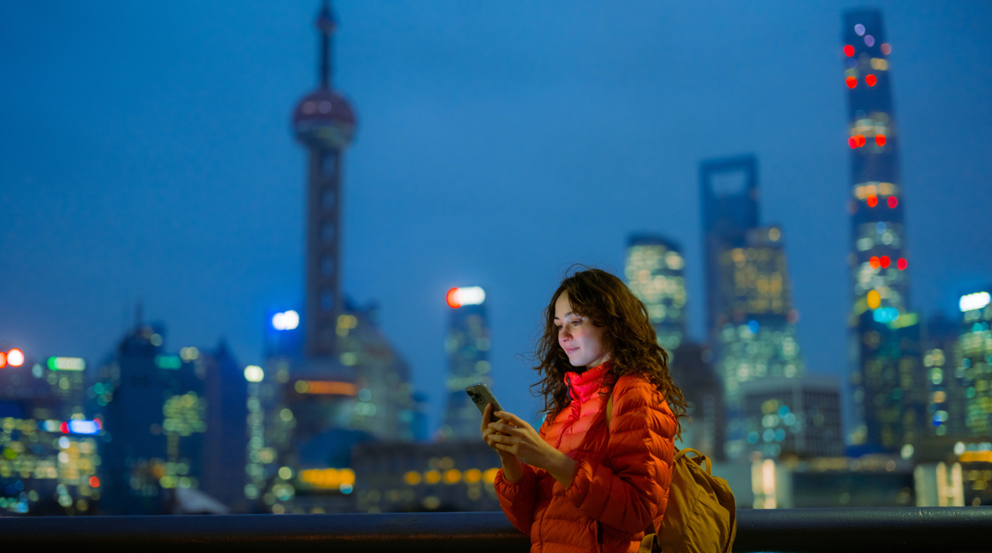 Junge Touristin steht abends vorm Shanghai Tower mit Internet in China