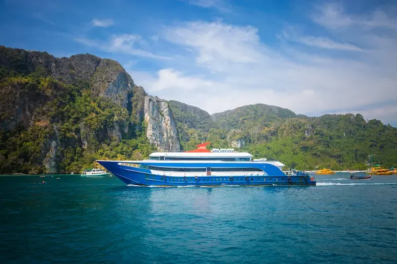 A ferry sailing past tree-covered limestone cliffs in Thailand.