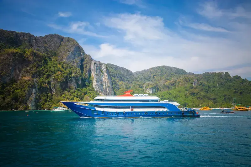 A ferry sailing past tree-covered limestone cliffs in Thailand.