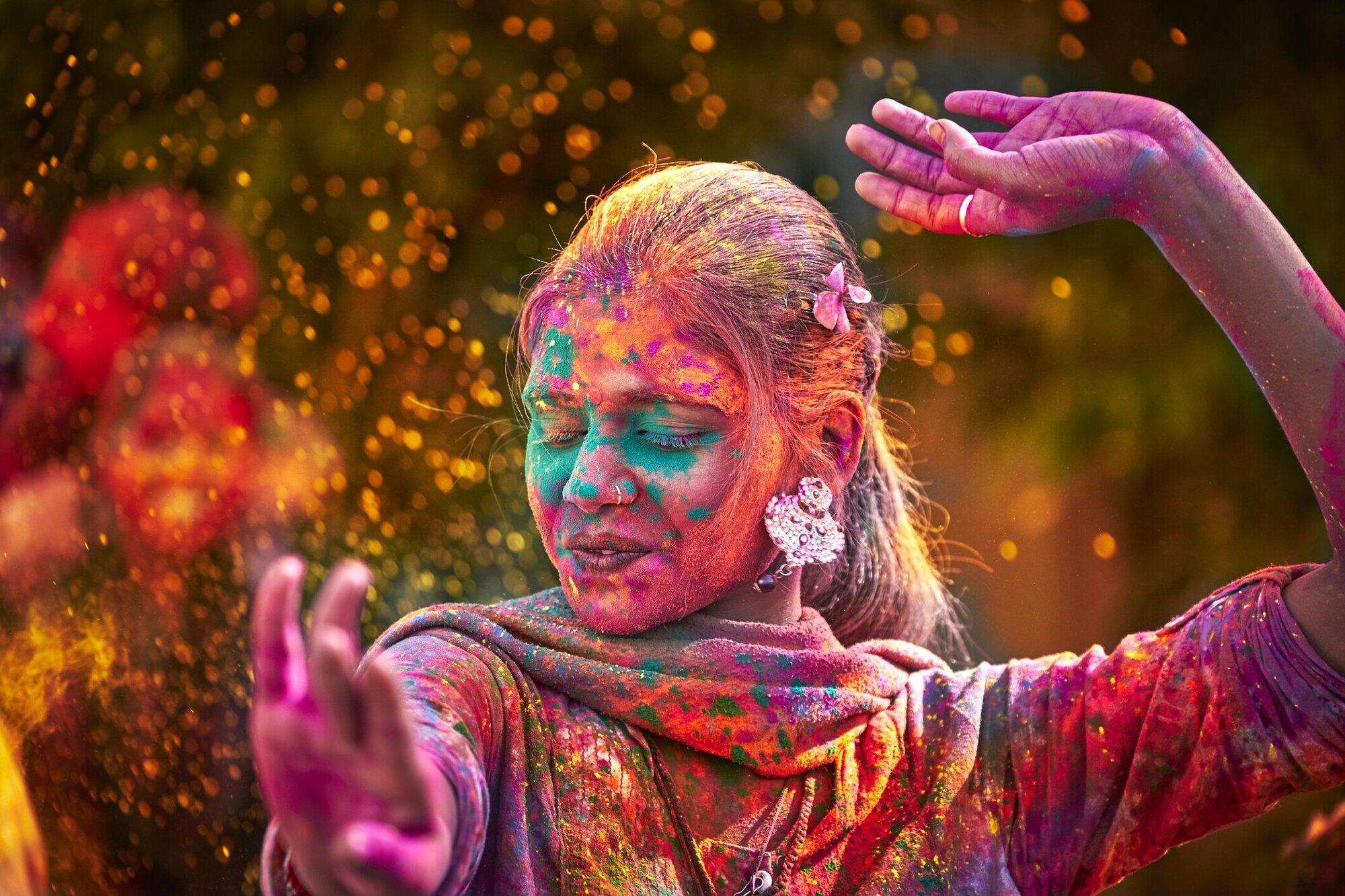 Eine Frau mit bunten Farben im Gesicht tanzt beim Holi Fest in Indien