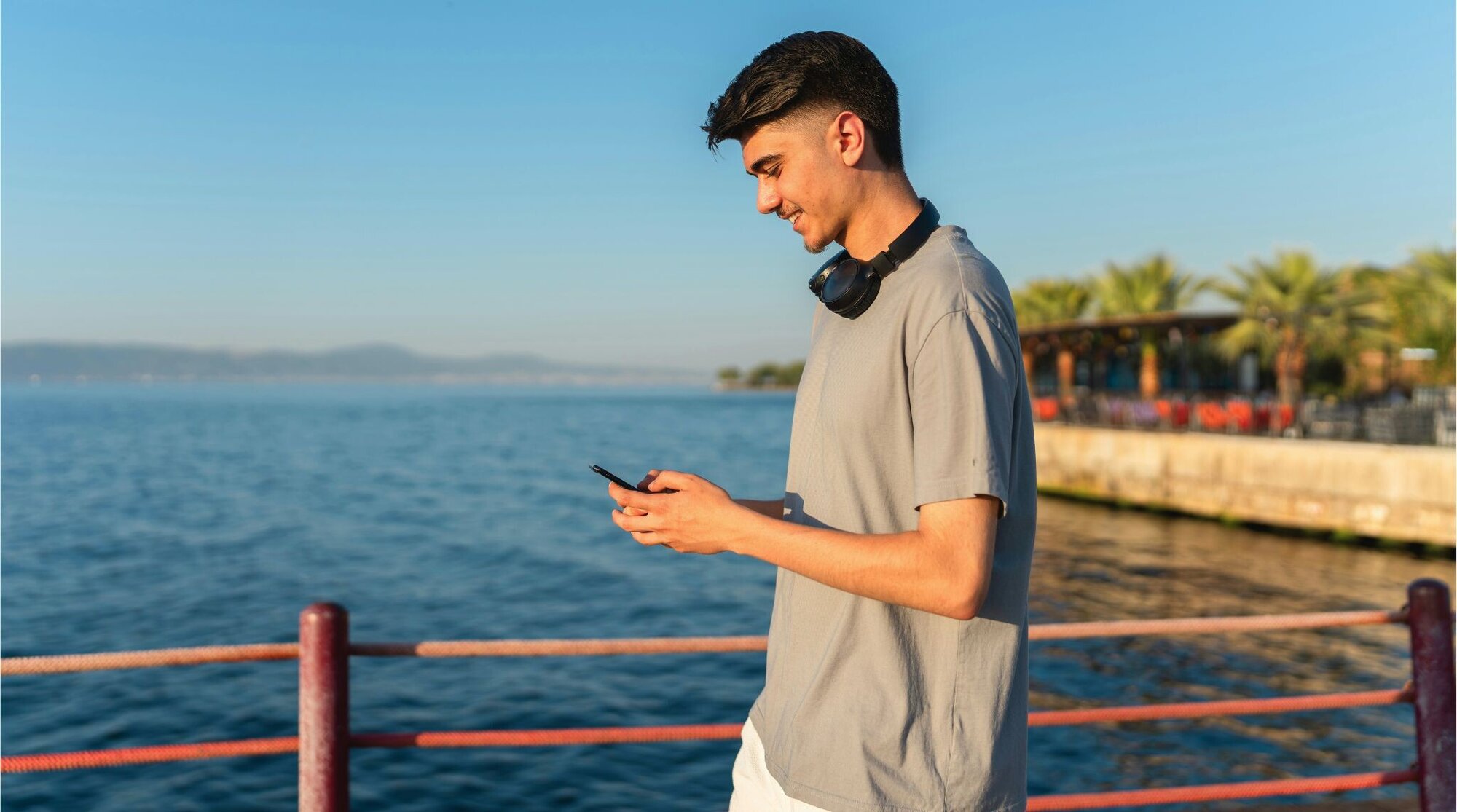 Homem jovem à beira-mar olhando o celular.