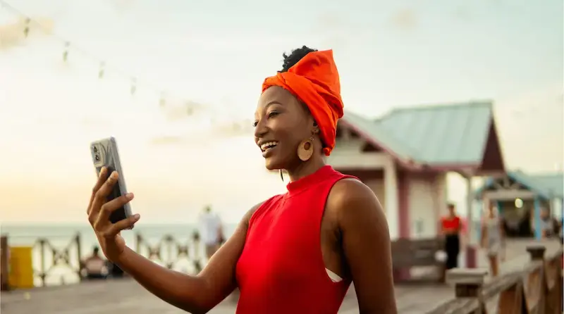 Mujer sonriendo mientras toma una selfie con su teléfono en un muelle al atardecer durante un viaje