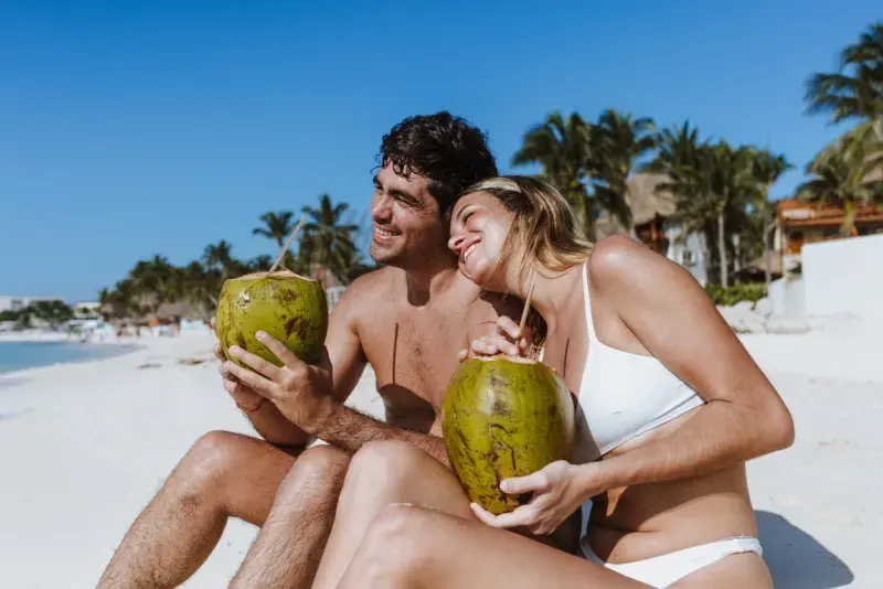 Pareja en la playa de Cancún bebiendo cocos, sin preocuparse por el costo del roaming en México