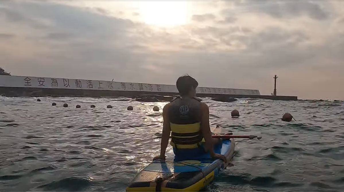 Man staring into a cloudy sunset while sitting on a standup paddleboard in the waters of Xiaoliuqiu