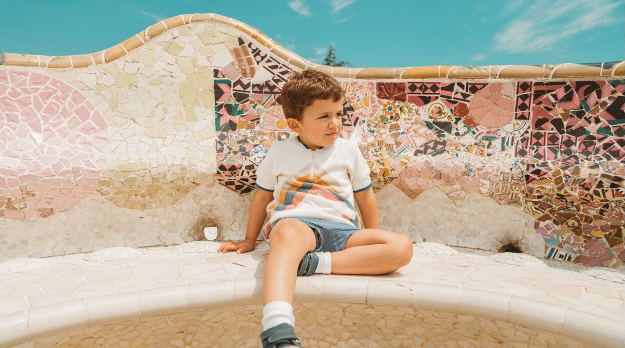 Niño sentado en los bancos de mosaico del Park Güell en Barcelona