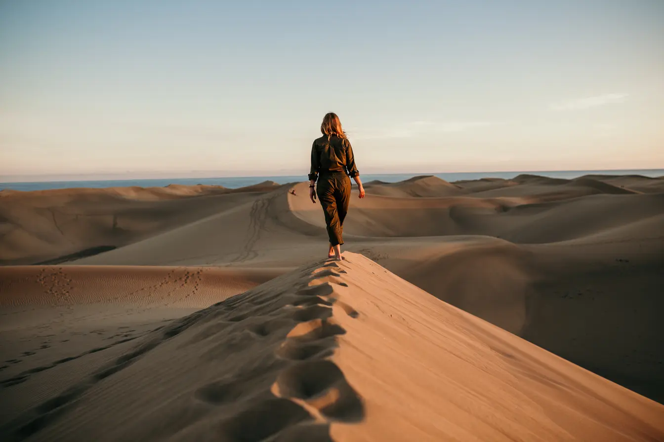Donna che cammina su una duna nel deserto in una giornata luminosa di maggio, ideale per un viaggio in Marocco.
