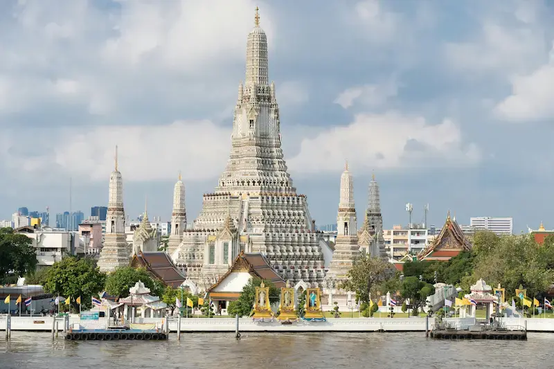 View of the riverfront Wat Arun temple with a tall central spire and four smaller stupas surrounding it.