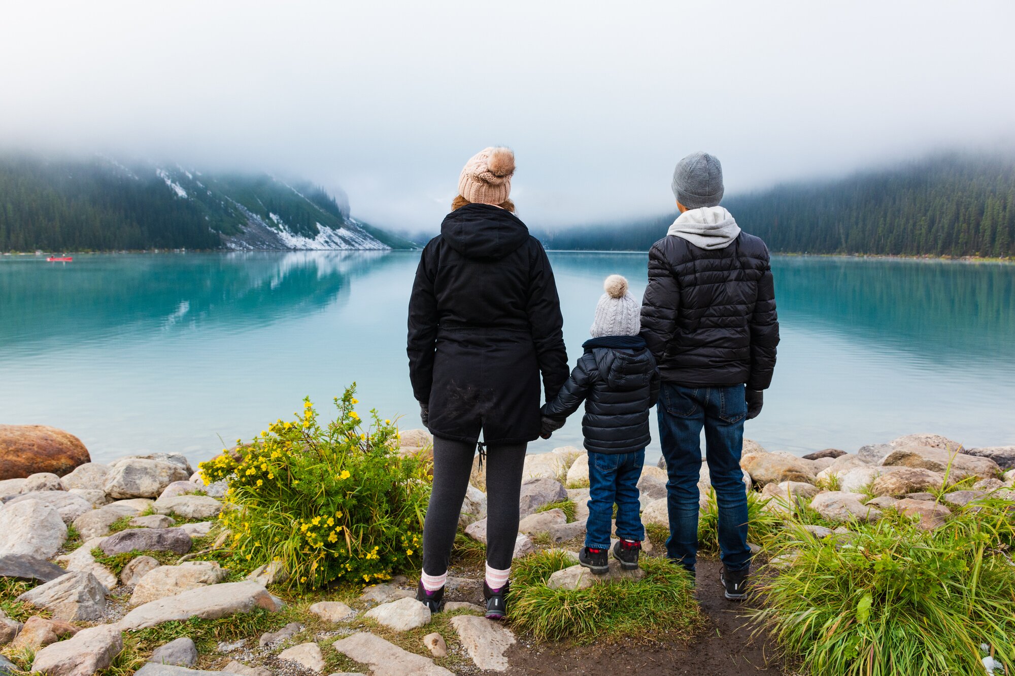 Famiglia in piedi in riva a un lago in Canada, esperienza immersa nella natura ideale per viaggi per famiglie