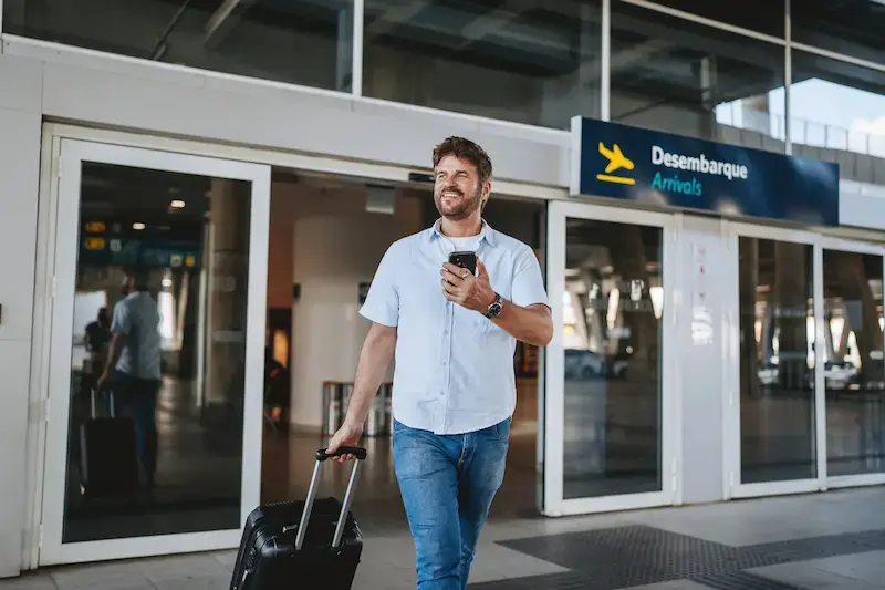 Viajero saliendo del aeropuerto con su teléfono móvil en Brasil.