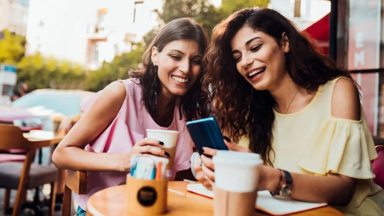 Duas meninas que se sentam em uma cafetaria e que olham um telefone, usando para dividir as contas.