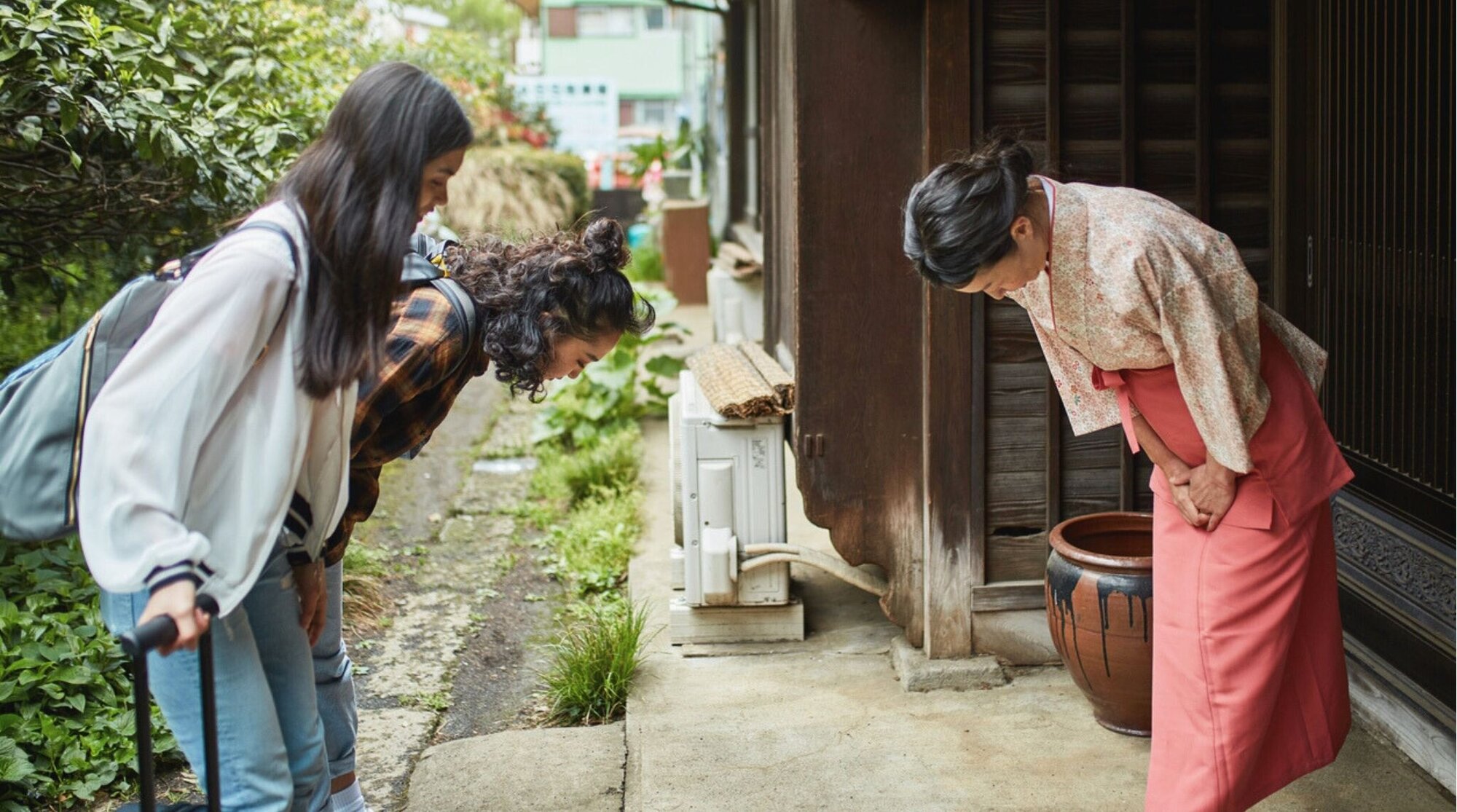 Anfitriona saludando a dos viajeras frente a un ryokan tradicional japonés.