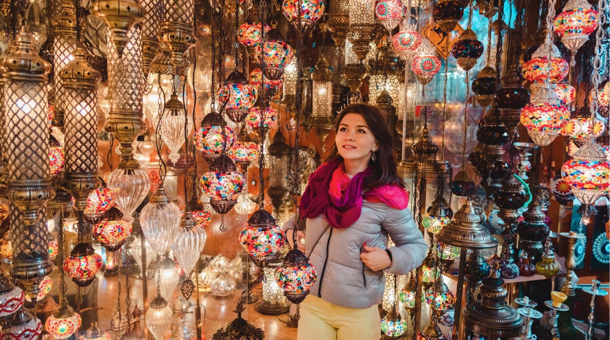 Mulher sorridente admirando lâmpadas turcas à venda no Grande Bazar, em Istambul, Turquia.