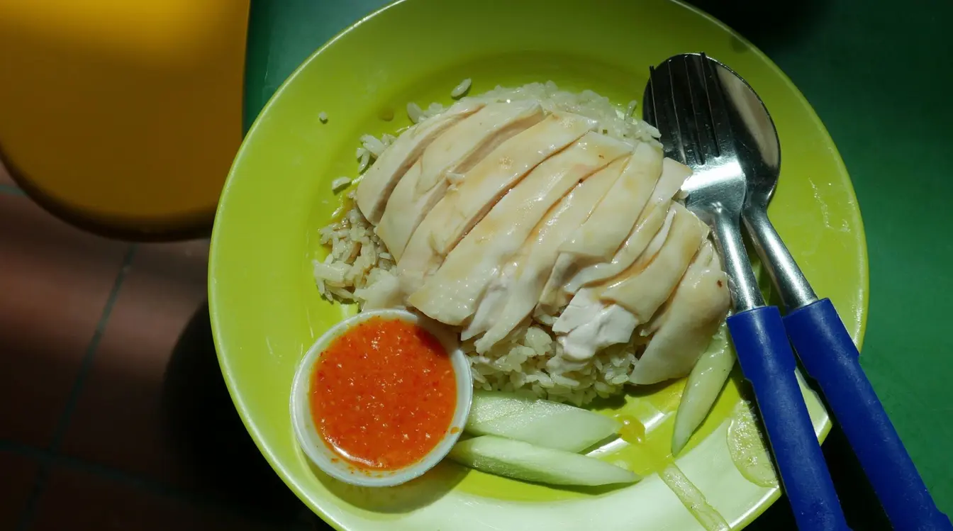 A plate of Hainanese chicken rice with chili sauce at a hawker center in Singapore.