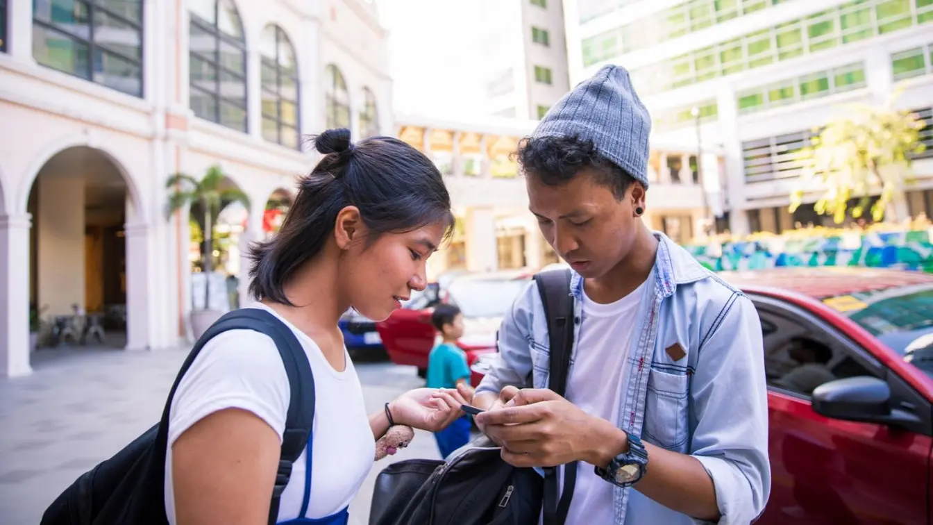 Two travelers using a smartphone on a street in the Philippines.