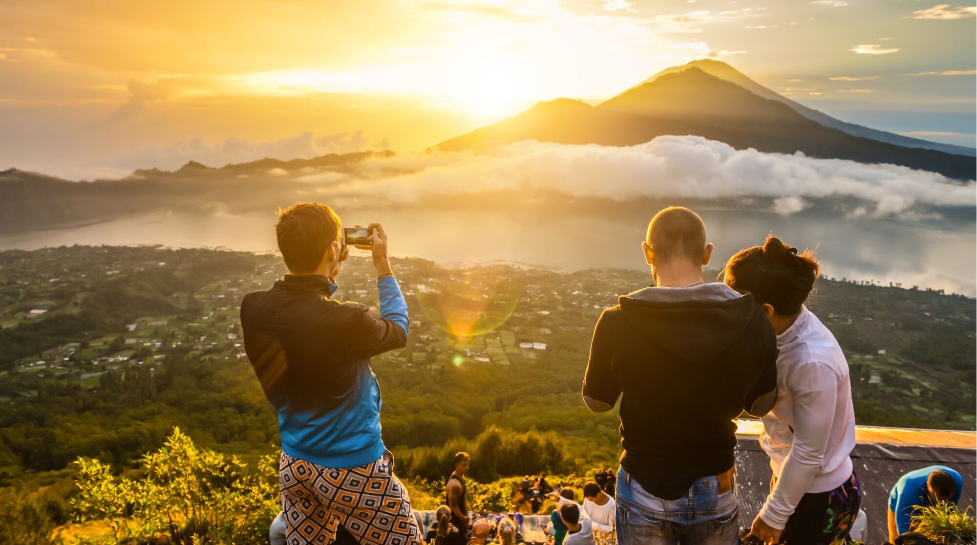 A group of tourists taking photos and watching the sun rise over Mount Batur in Bali.