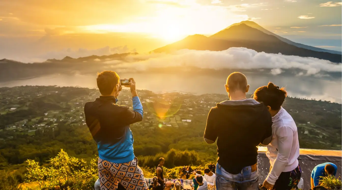 A group of tourists taking photos and watching the sun rise over Mount Batur in Bali.
