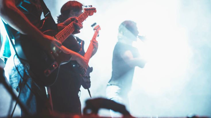 Two guitarists on stage with a singer in the background, symbolising the kind of scenes and atmosphere a travellers or visitor may expect when attending Summer Sonic Festival in Japan. 