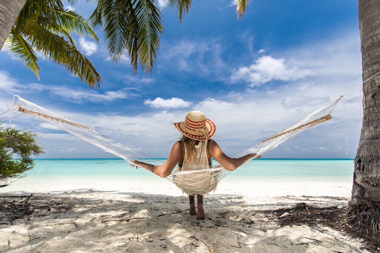 Vista posteriore di una donna che guarda la vista da un'amaca sulla spiaggia.