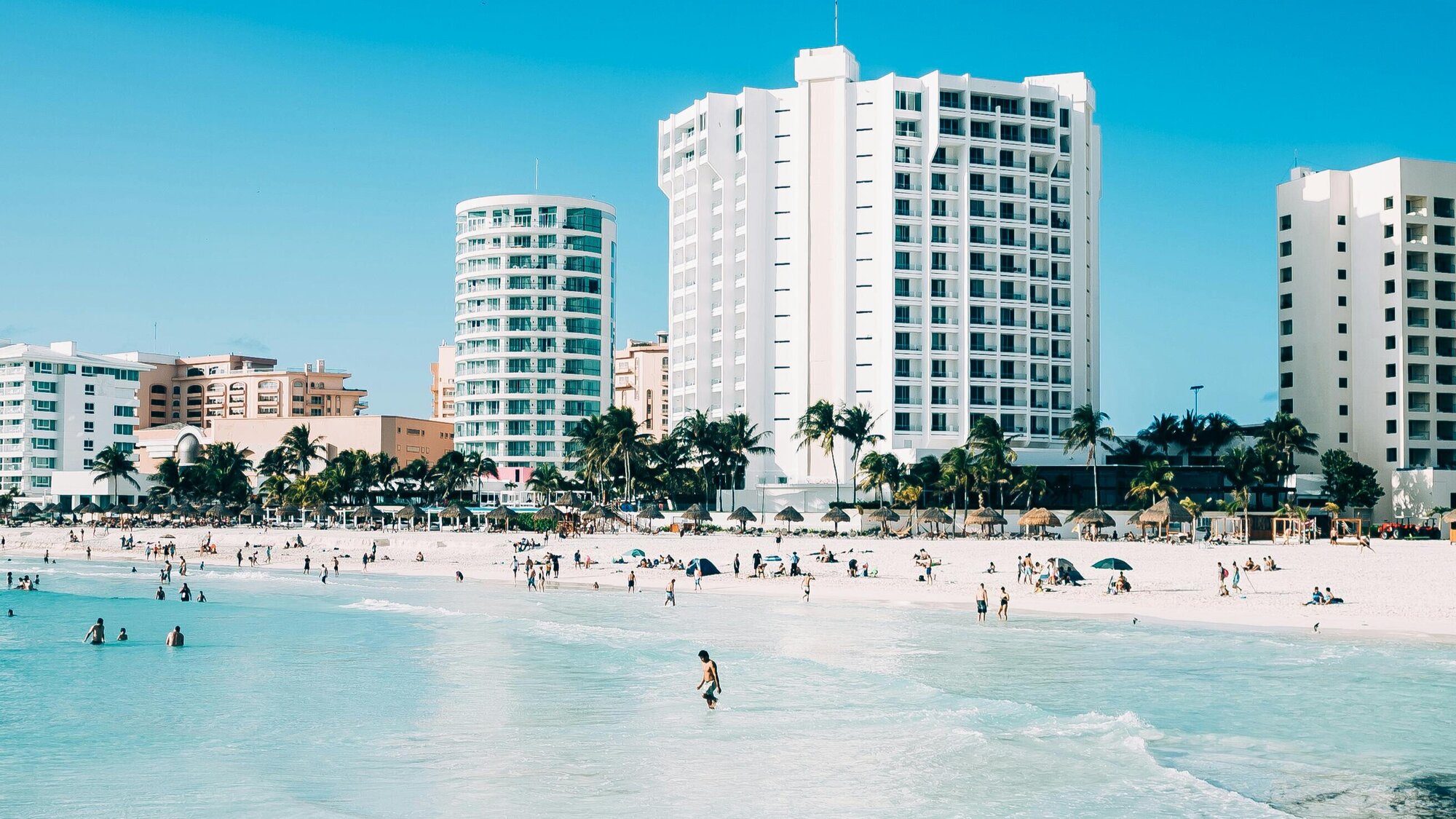 A busy beach in Cancun, Mexico, showing bright blue water and people lounging on the sand