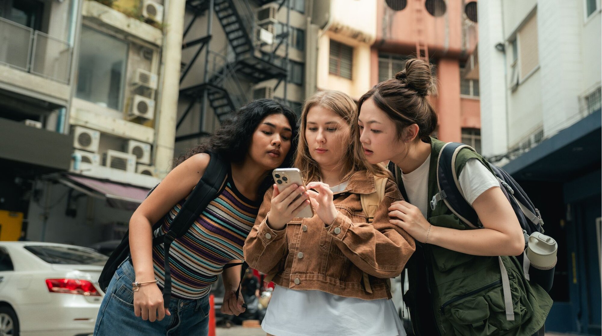Grupo de amigos reunidos em torno de um smartphone, olhando para o mapa na tela enquanto navegava pela cidade.