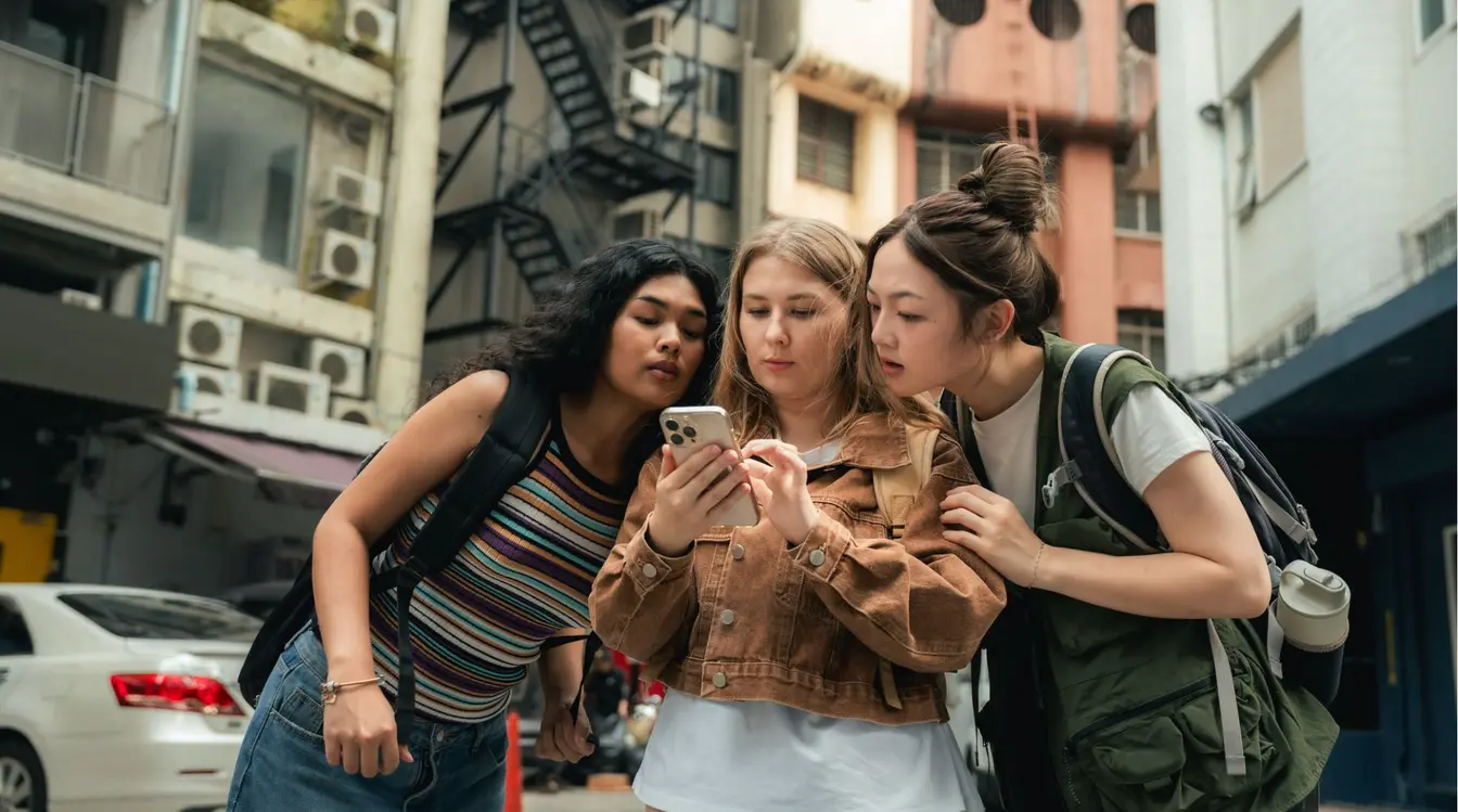 Grupo de amigos reunidos em torno de um smartphone, olhando para o mapa na tela enquanto navegava pela cidade.