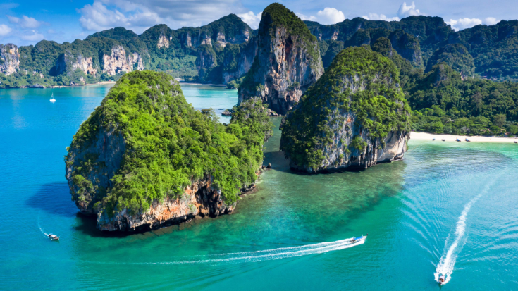 An image of an aerial view of Phra Nang Cave Beach in Thailand, with traditional long tail boats on Ao Phra Nang Beach near Railay Bay, Krabi, Thailand, to illustrate a blog post entitled '33 Fun Facts about Thailand'.