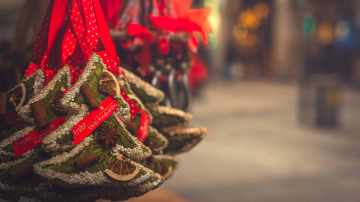 A close-up image of some hand-made baubles in the shape of Christmas trees, in bunches, with red ribbons holding them up to illustrate a blog post entitles the Best Christmas Markets in the UK for 2024.
