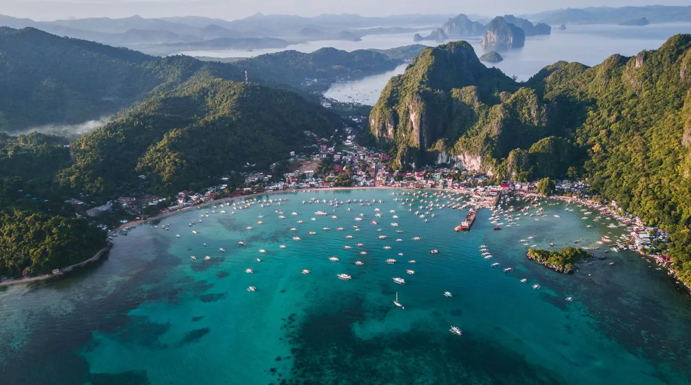 Aerial view of boats in the water and lush karst mountains surrounding El Nido on Palawan Island in the Philippines.