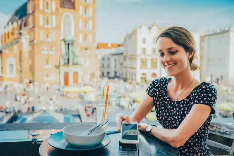 Viajera sentada en una terraza pagando la cuenta con su celular