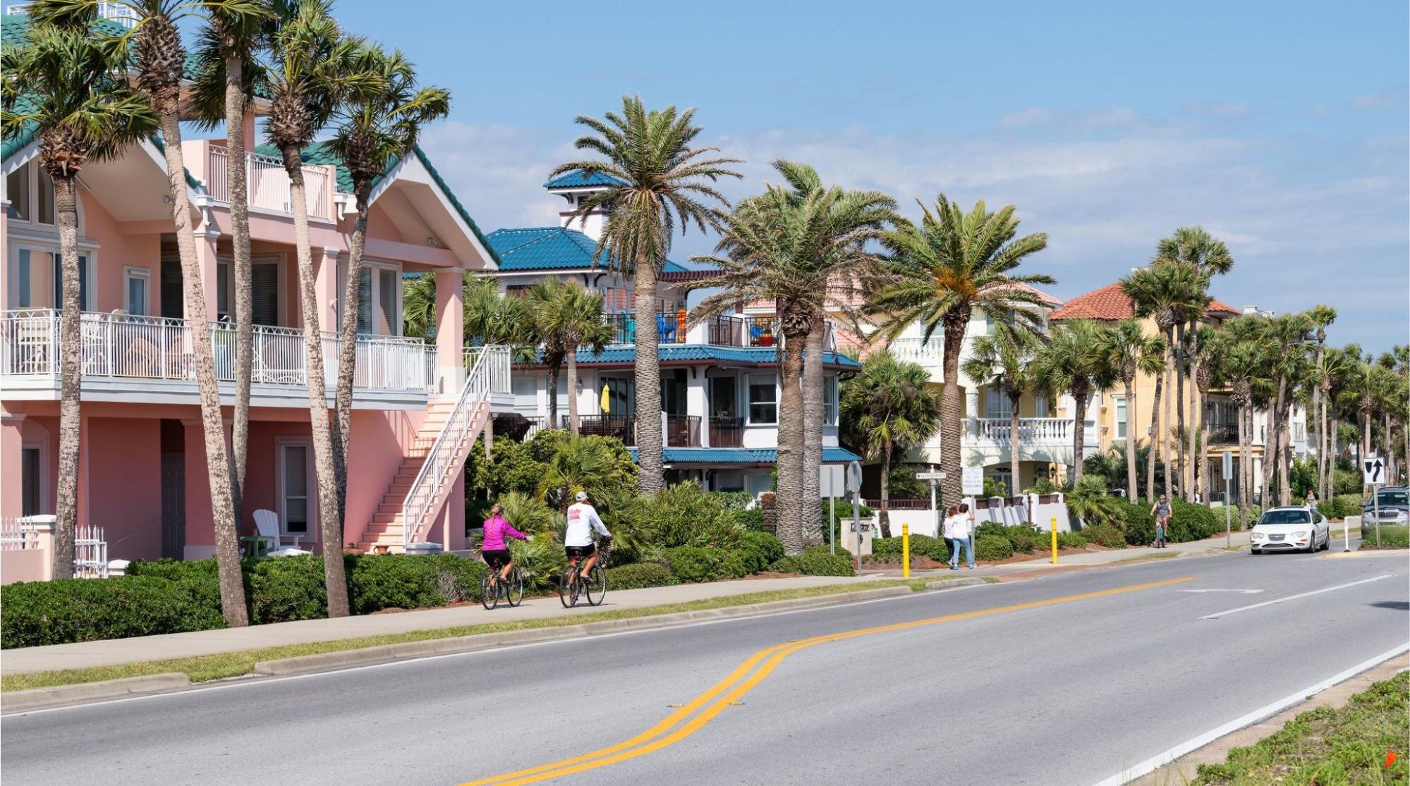 Rua residencial tranquila em Miramar, na Grande Miami, com casas de fachada colorida, palmeiras e moradores andando de bicicleta em um dia ensolarado.