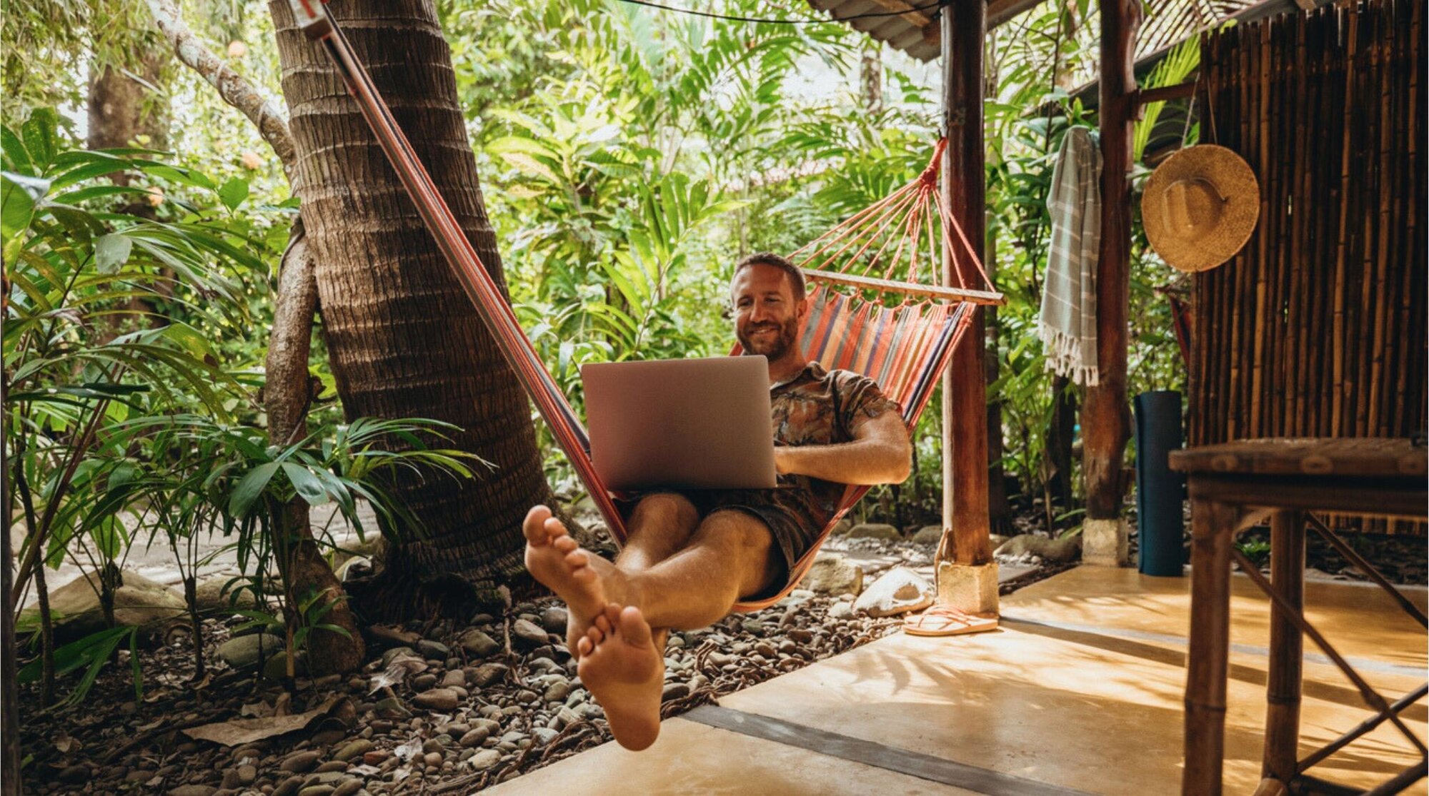 Hombre trabajando en su laptop mientras descansa en una hamaca en un entorno tropical de Costa Rica.