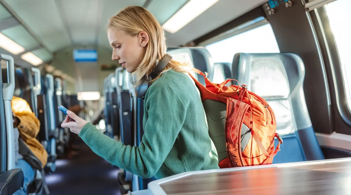 A woman with a backpack using a smartphone while sitting on a train seat.