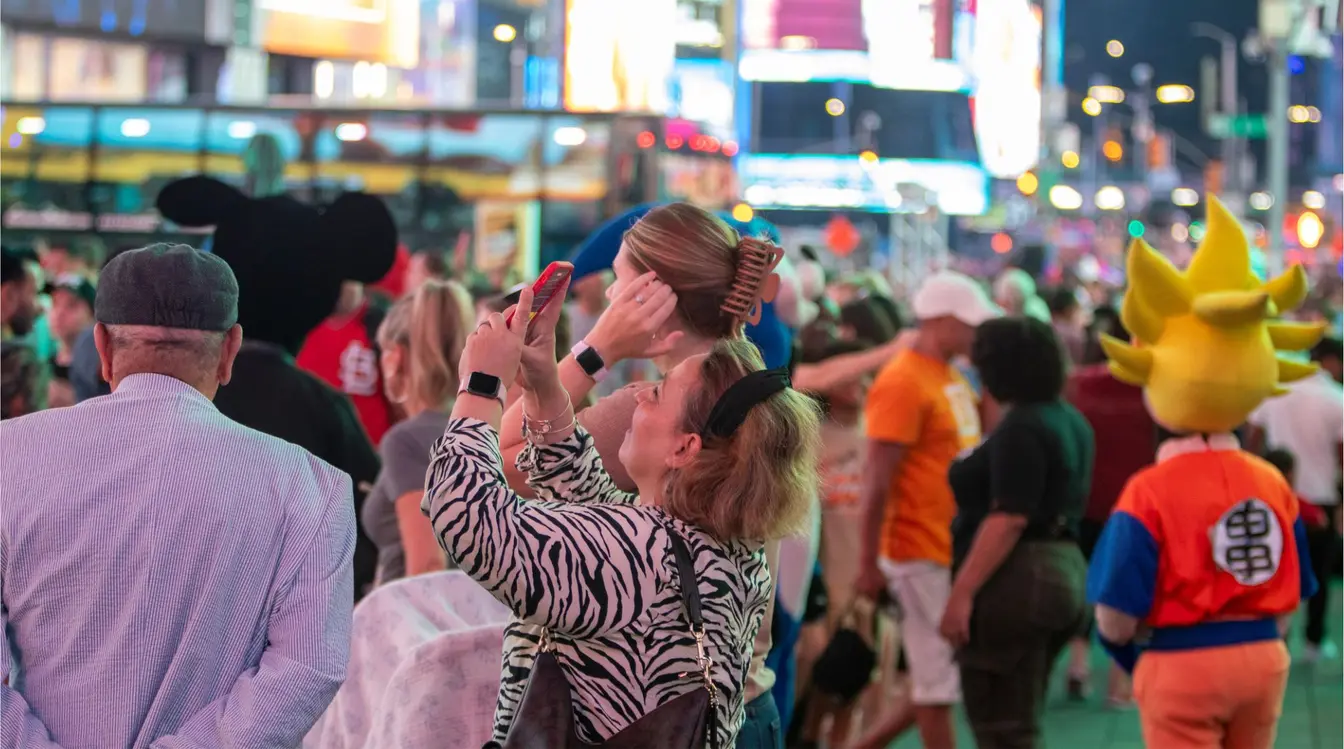 Turistas tirando fotos de letreiros e artistas de rua fantasiados de personagens populares na movimentada Times Square à noite.