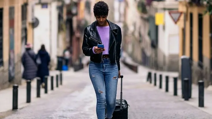 Uma mulher caminha pela rua, carregando malas e usando o eSIM Ilimitado no celular para se orientar.