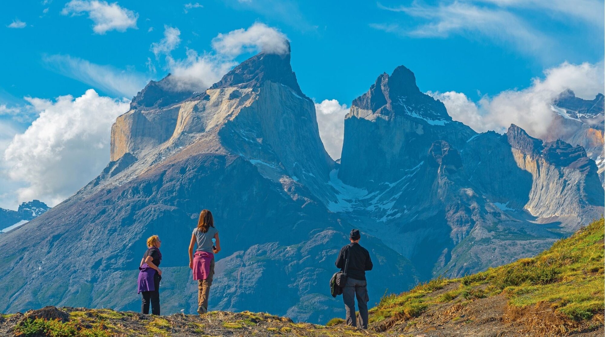 Três turistas em uma aventura de trekking no Parque Nacional Torres del Paine, observando os picos andinos do Cuernos del Paine, Patagônia, Chile.