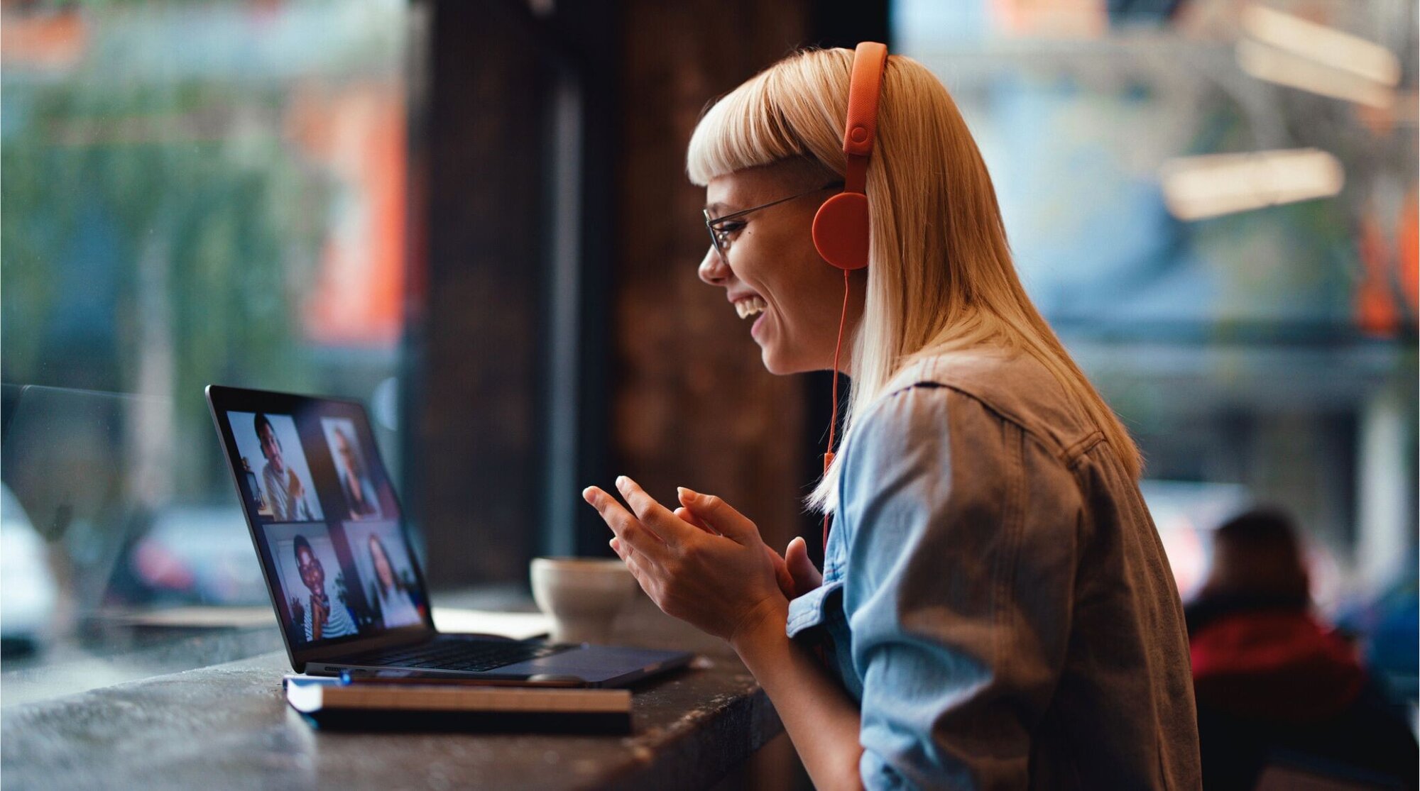 Una joven mujer participando en una reunión en línea desde su laptop en una cafetería.