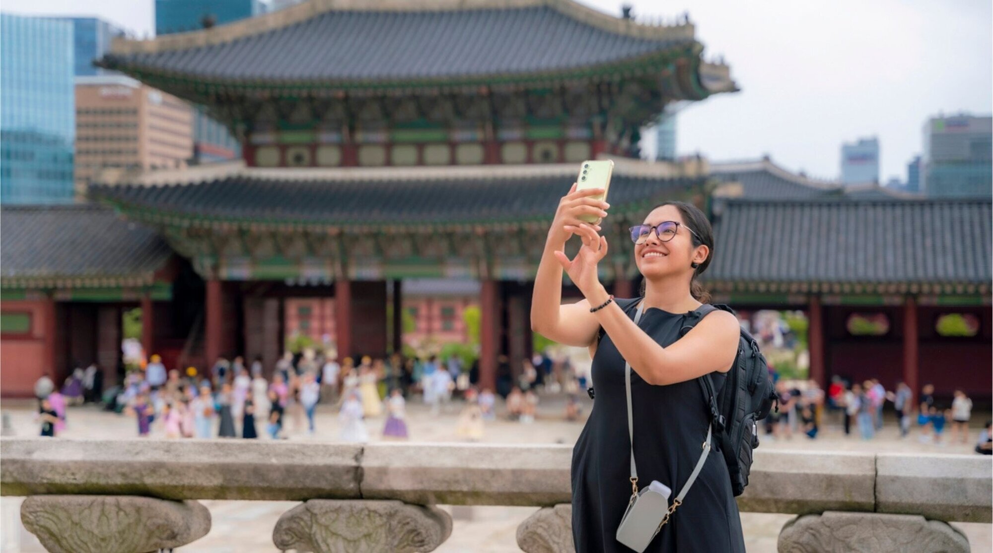 Jovem mulher latina feliz em um vestido preto admirando a arquitetura tradicional e tirando selfie no Palácio Gyeongbokgung, Coreia do Sul.