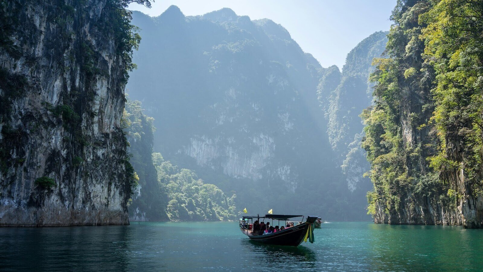 A boat with several people on a body of water surrounded by tall mountains and trees during daytime