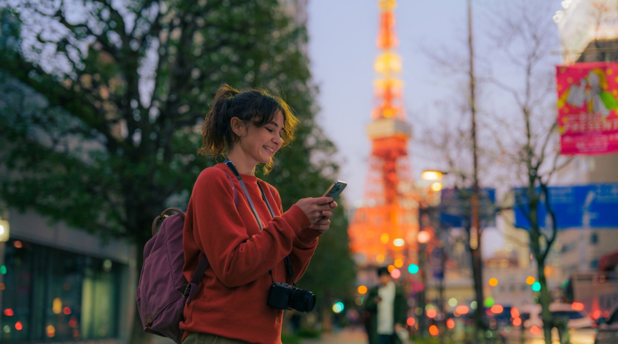 Eine Frau steht mit Smartphone in der Nähe des Tokyo Tower in Japan und benutzt Apps