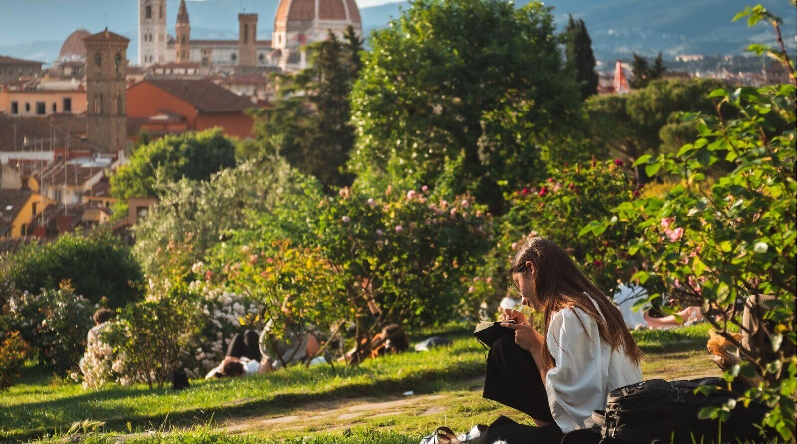 Menina sentada na grama com uma bela vista de Florença ao fundo, aproveitando o clima na Itália na primavera.